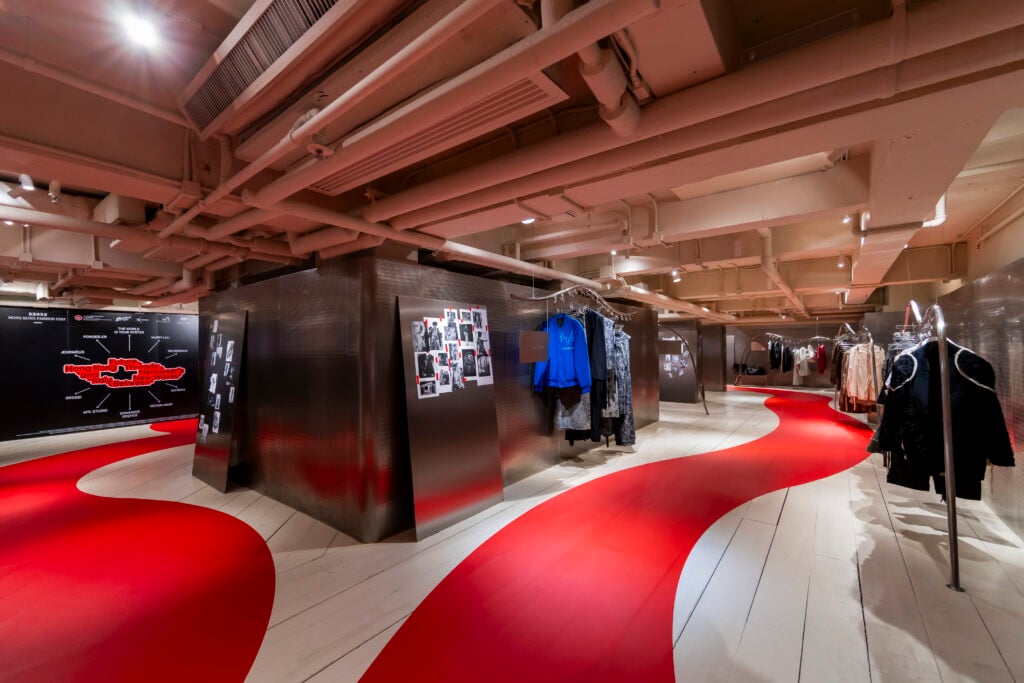 Future Threads exhibition interior featuring suspended menswear designs, metallic display structures and a red exhibition walkway.